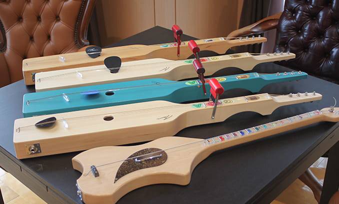 5つの細長いギターに似た木製のカラフルな楽器がテーブルの上に並んでいる